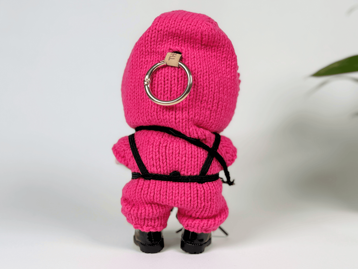 Back view of crochet Squid Game guard outfit on Labubu doll showing detailed black harness and pink hoodie with keyring