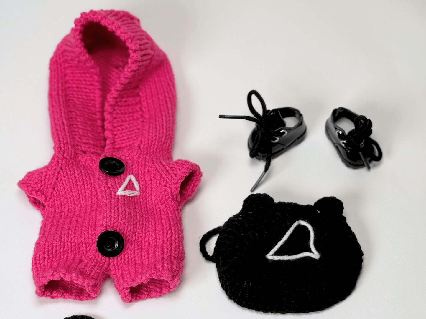 Close-up flat lay of Squid Game crochet costume set for Labubu with pink jumpsuit, triangle mask, vinyl boots, and accessories