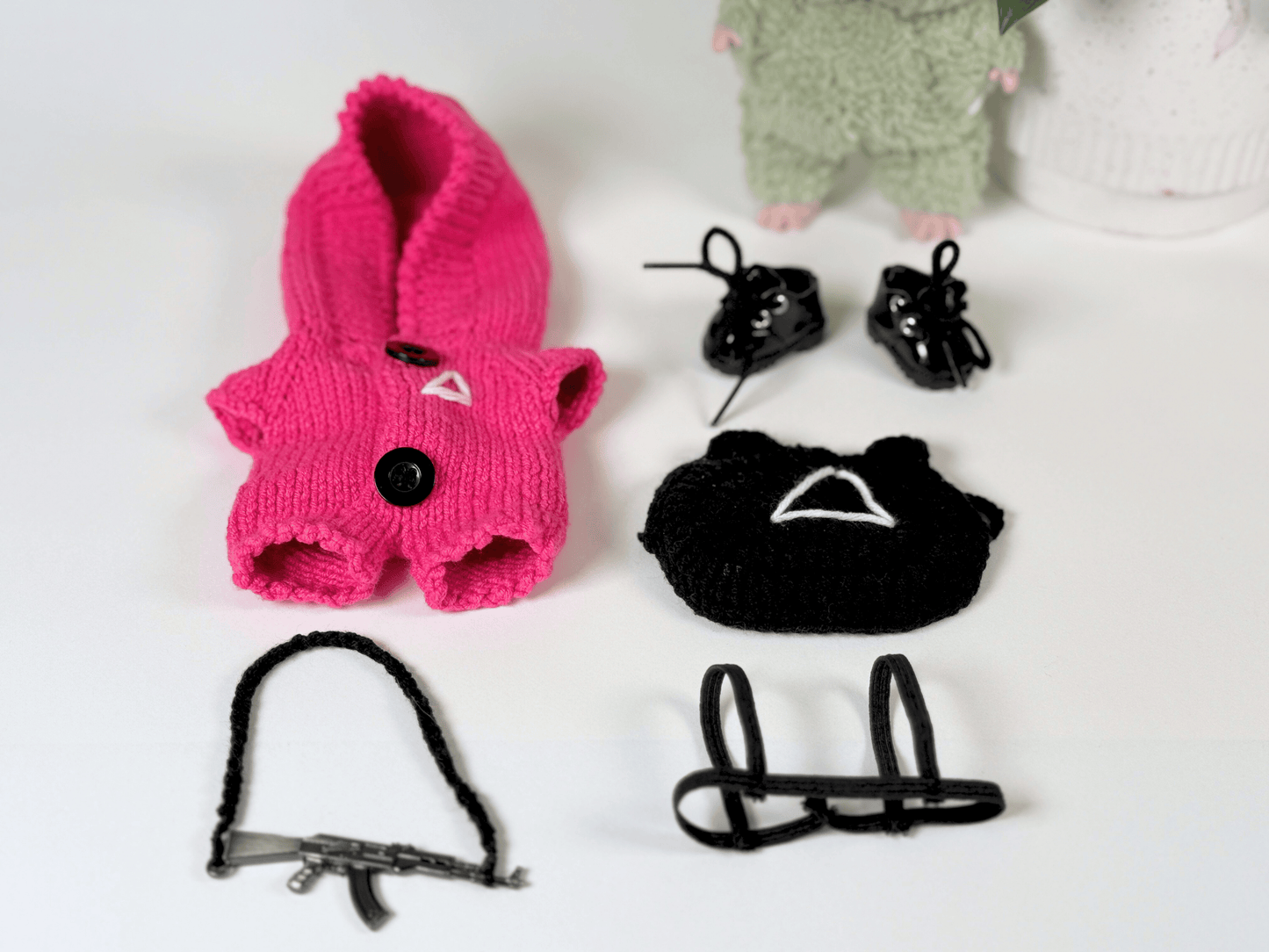 Flat lay of complete handmade Squid Game Labubu guard outfit including pink jumpsuit, black mask, gun with strap, and boots