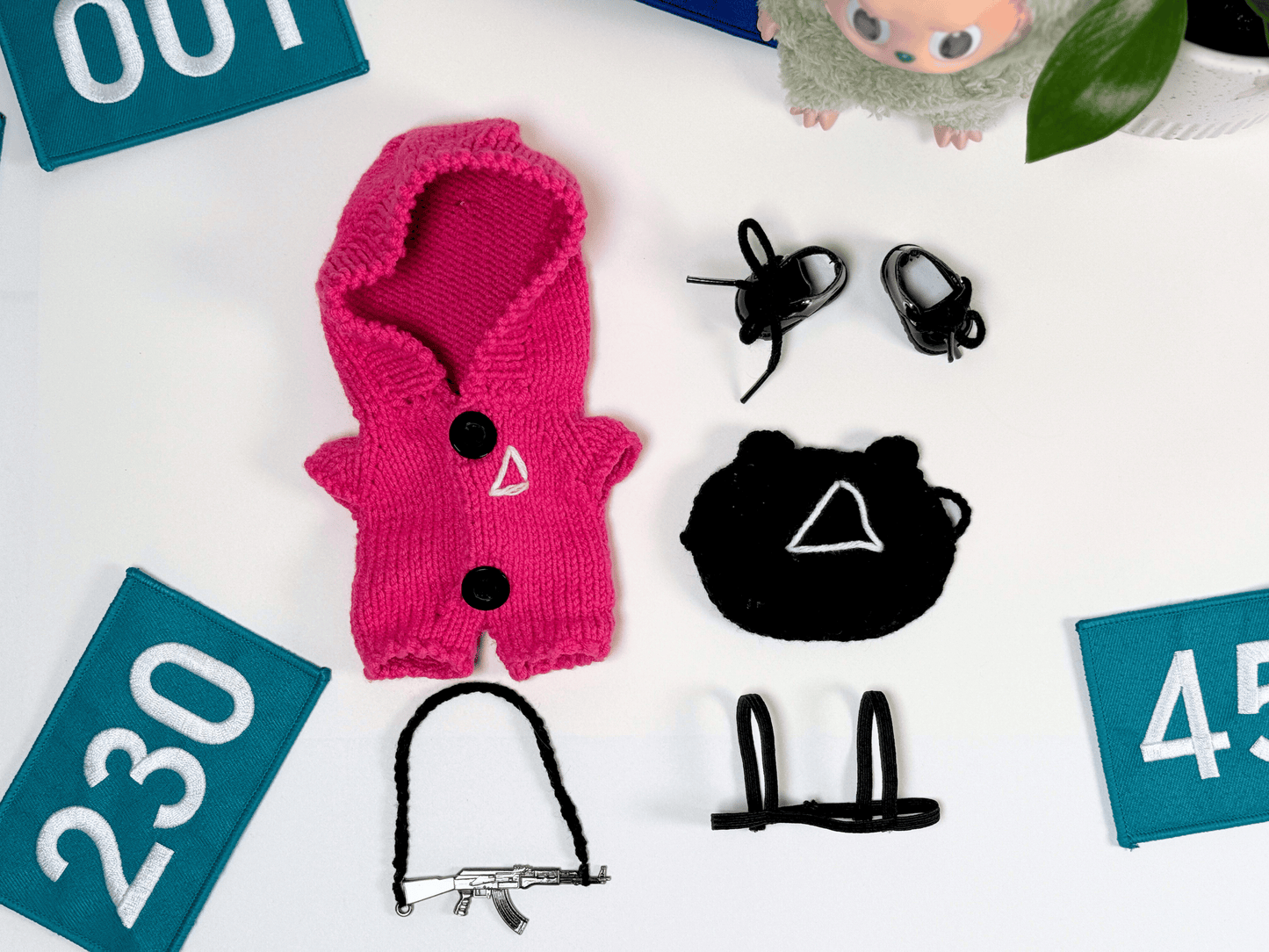 Full handmade Labubu pink guard outfit laid out with Squid Game number patches, pink jumpsuit, triangle mask, gun and harness