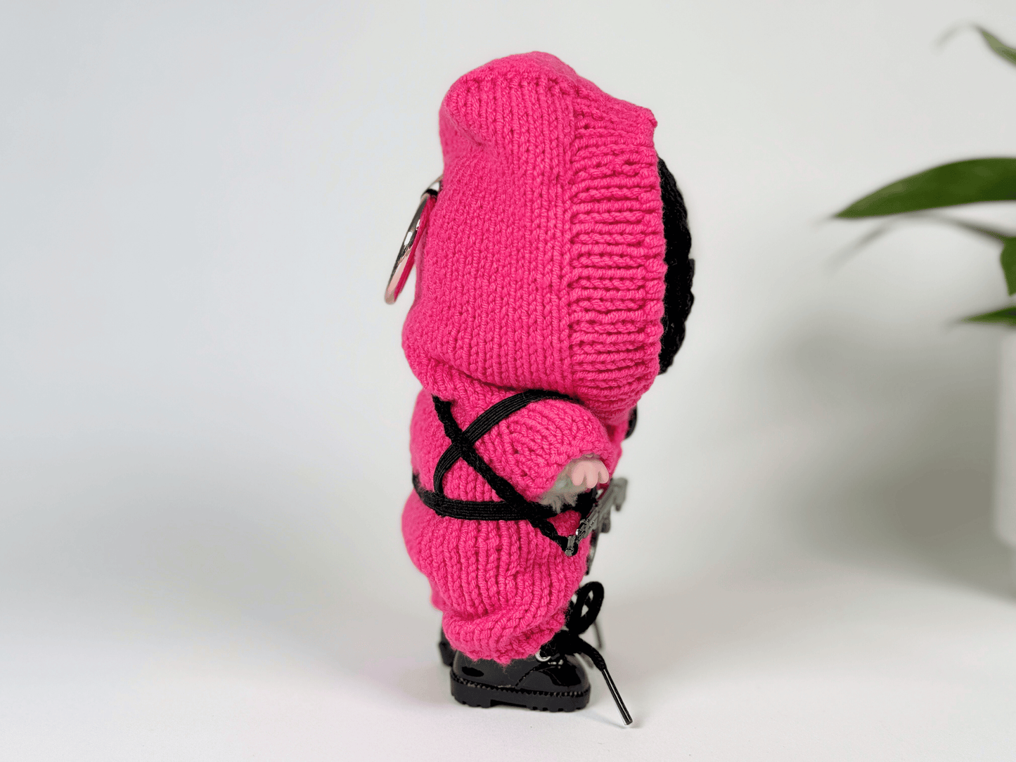 Side view of Labubu doll wearing handmade Squid Game pink guard crochet costume with elastic harness and mini gun prop