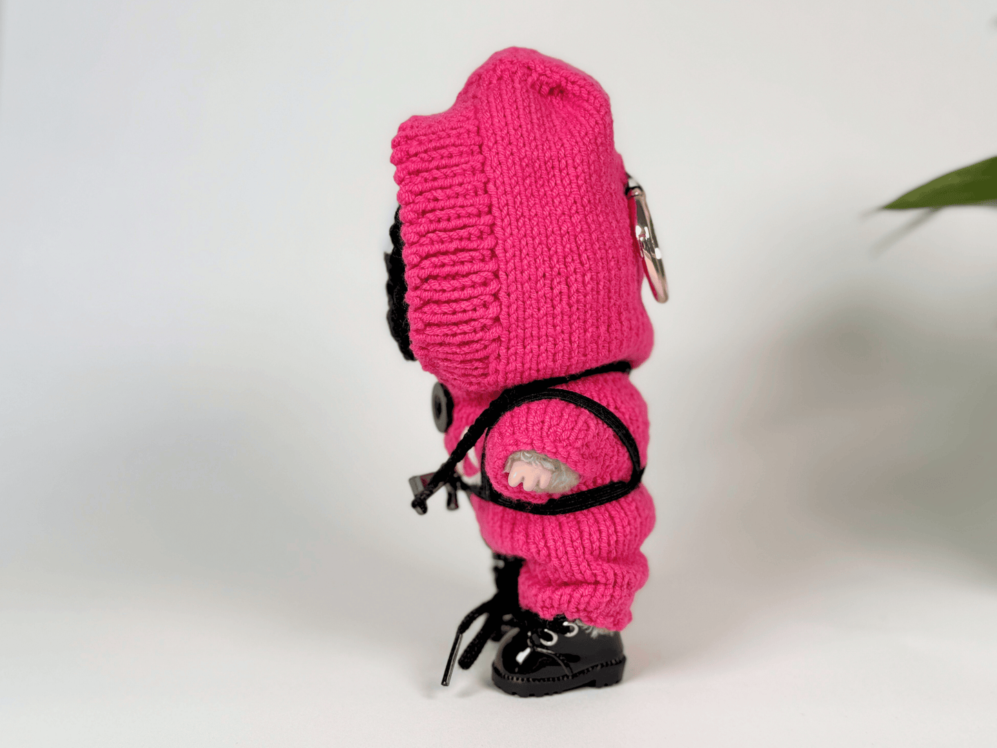 Side profile of Labubu doll dressed in handcrafted Squid Game pink guard jumpsuit, triangle face mask, and lace-up boots
