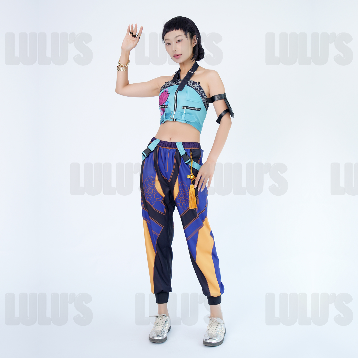Female model wearing K-Pop Demon Hunters Zoe cosplay costume, blue floral crop top with zipper and purple gold pants, styled with character accessories.
