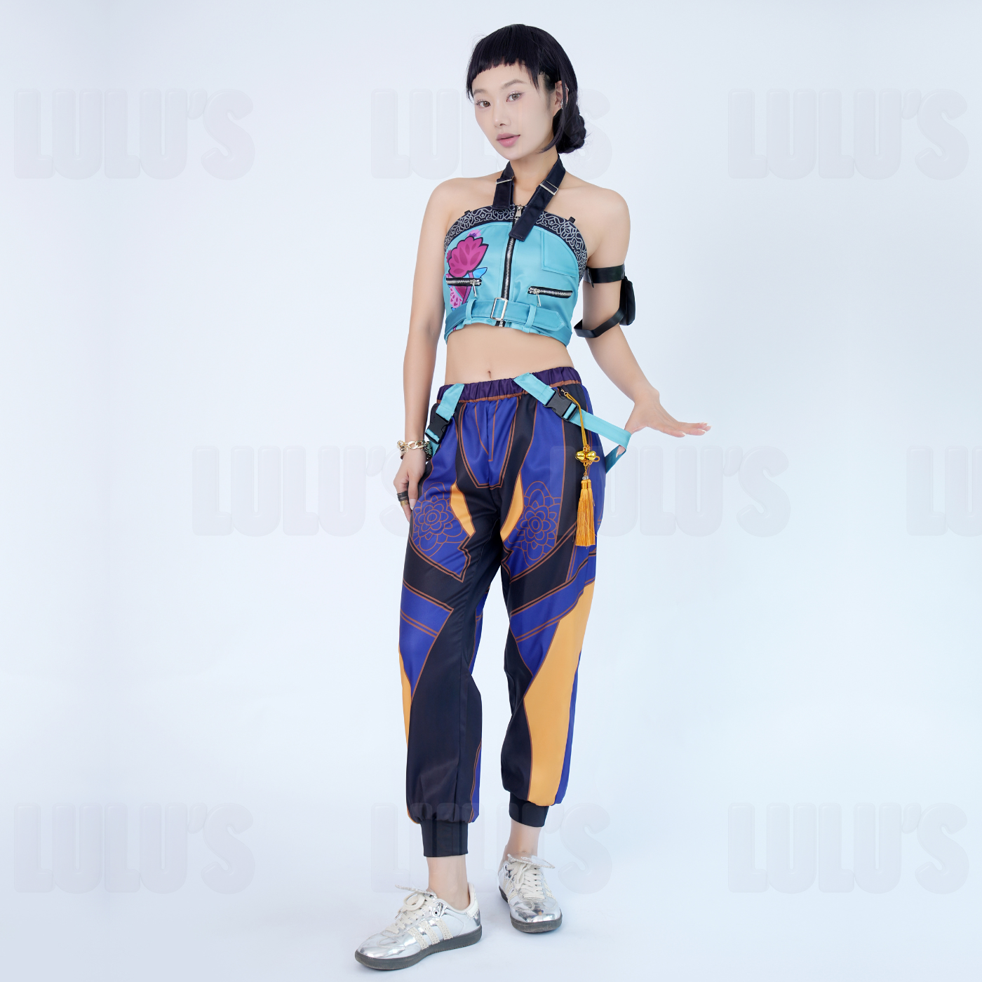 Model in K-Pop Demon Hunters Zoe cosplay costume striking character pose, featuring blue crop top, purple patterned jogger pants, tassel belt, and black arm band.