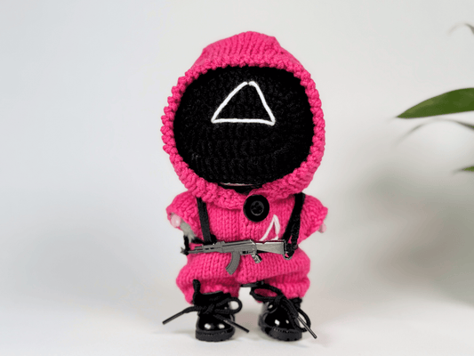 Crocheted toy figure in a pink outfit with a black mask on a white background