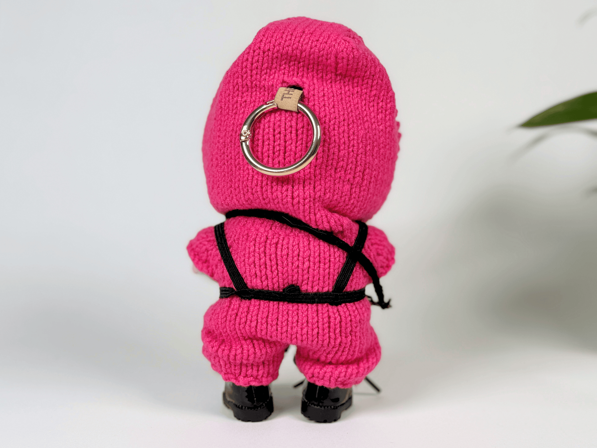 Back view of crochet Squid Game guard outfit on Labubu doll showing detailed black harness and pink hoodie with keyring