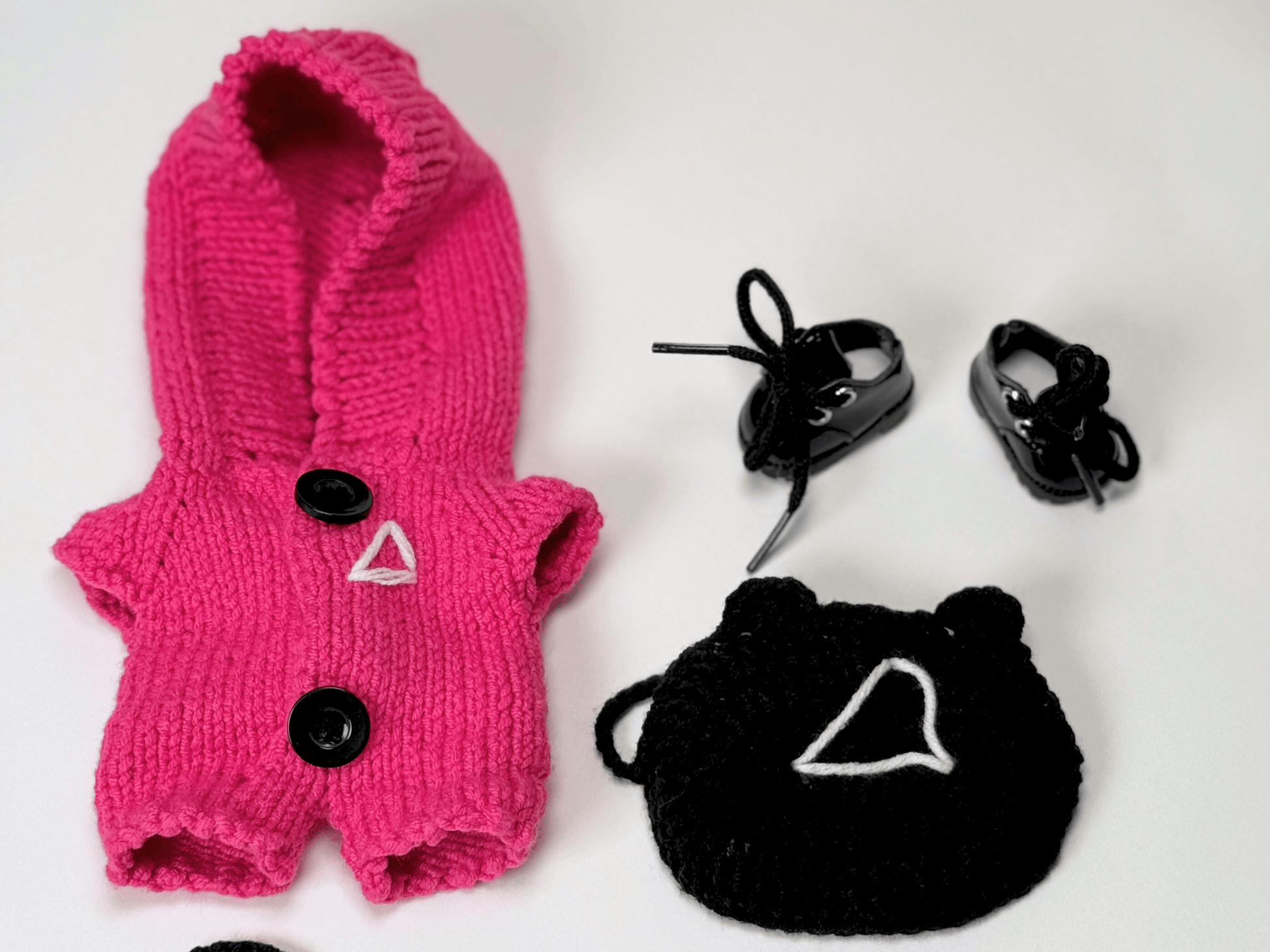 Close-up flat lay of Squid Game crochet costume set for Labubu with pink jumpsuit, triangle mask, vinyl boots, and accessories