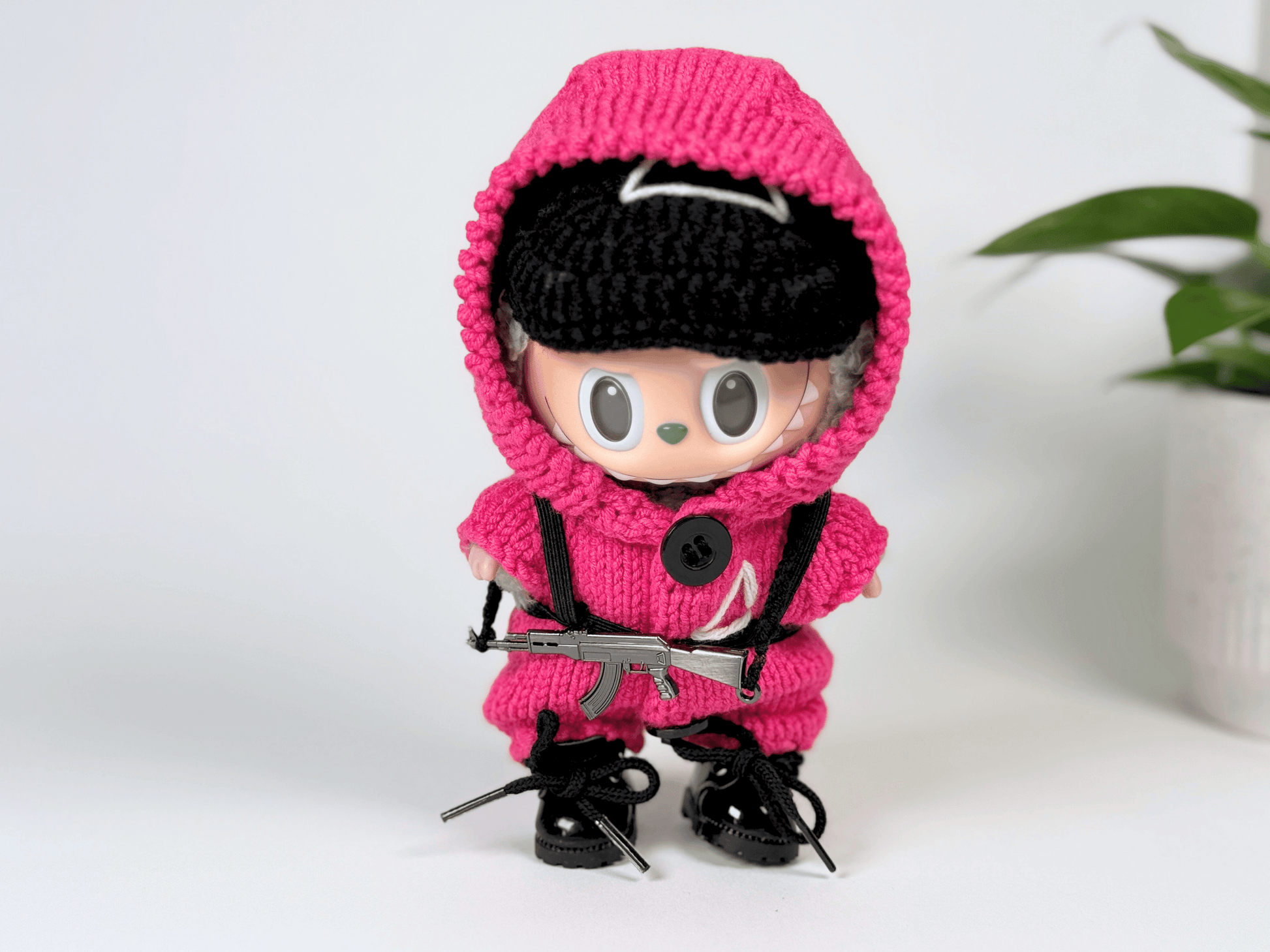 Labubu doll with mask lifted, showing face while wearing complete handmade Squid Game pink guard outfit and accessories