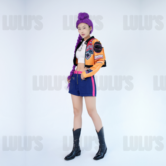 Female model in K-Pop Demon Hunters Rumi cosplay costume wearing orange cropped jacket, purple wig, navy shorts, black boots, and silver accessories in full-body pose.